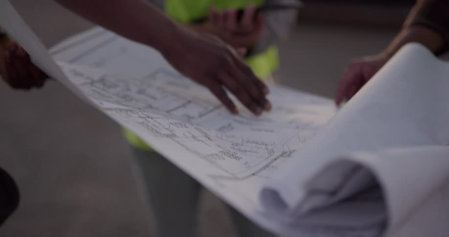A group of construction workers look at a blueprint while holding it between them