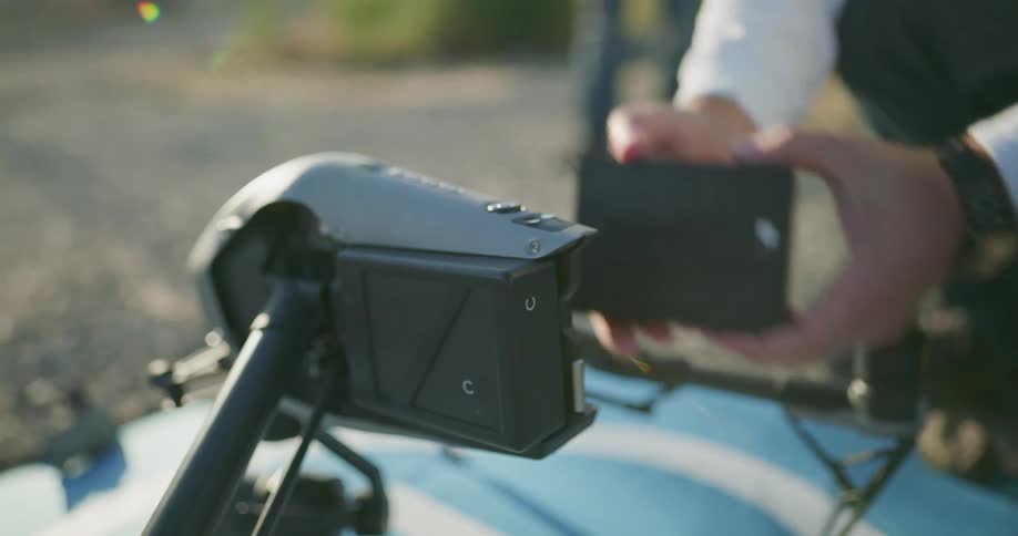 A person putting batteries on a drone with plants and dirt in the background