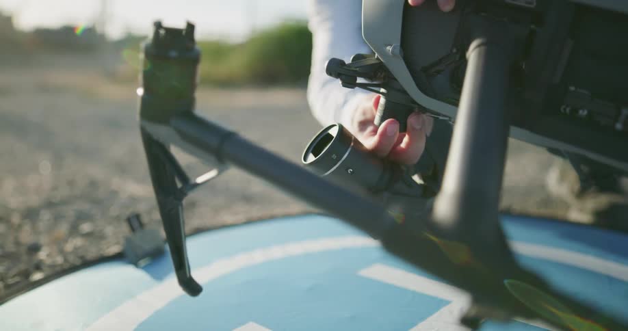 A person putting a camera on a drone with plants and the sky in the background