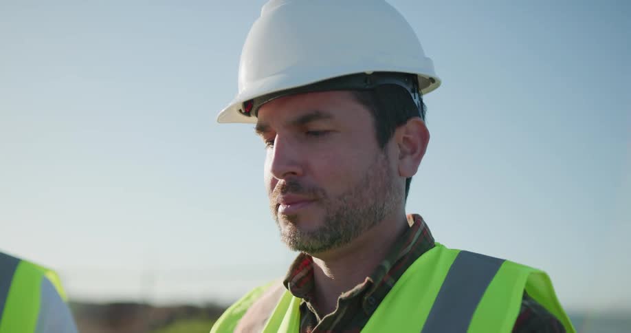 Construction worker wearing a white hard hat and yellow vest at a construction site