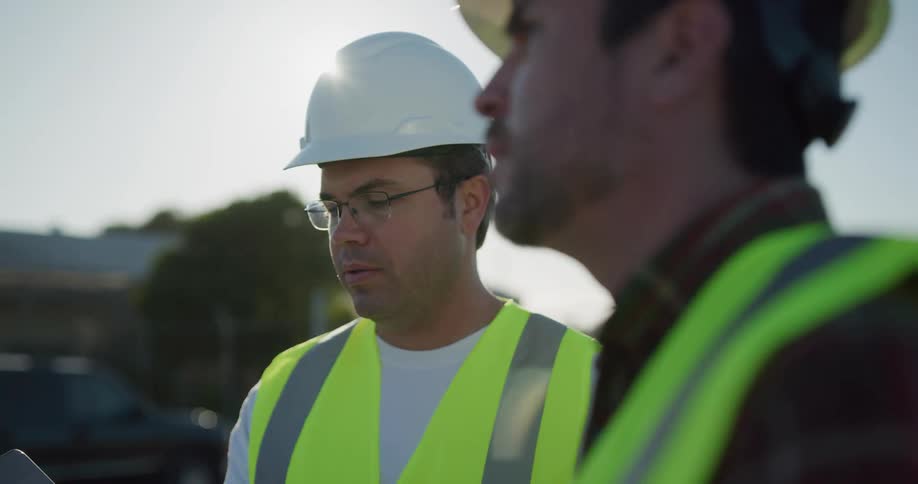Two men with hard hats and vests with the sky and clouds in the background