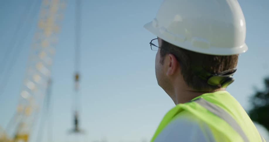 A man with a hard hat and vest with the sky and a construction crane in the background