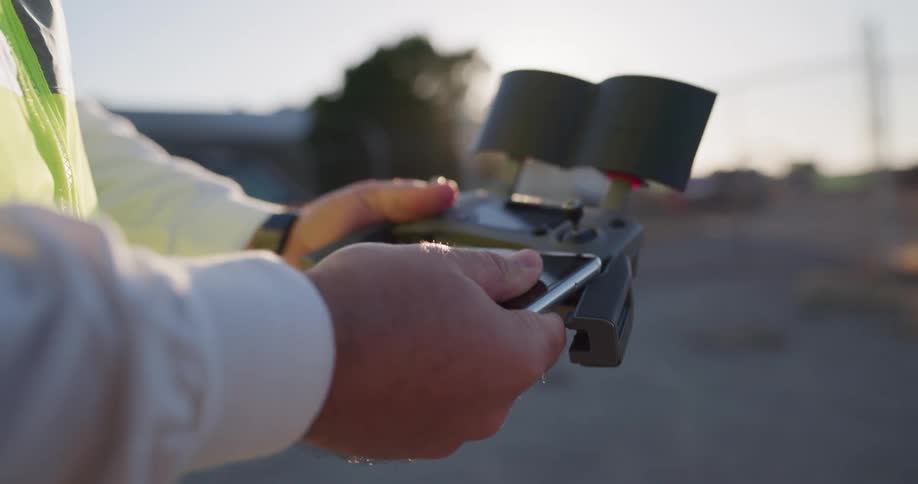 A man inserts his smartphone into a radio controller for a drone while standing outdoors during the day