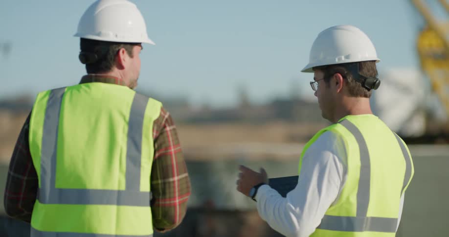 Two men in hard hats fly a drone over a construction site
