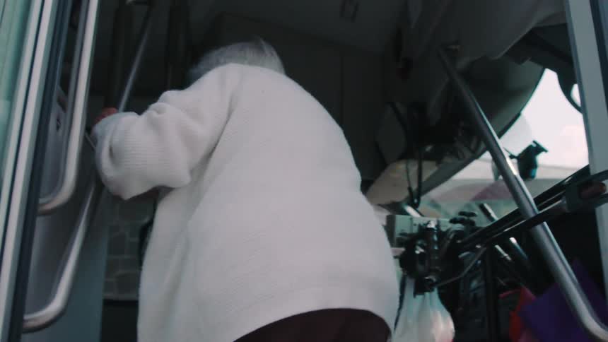 An elderly woman boards a bus