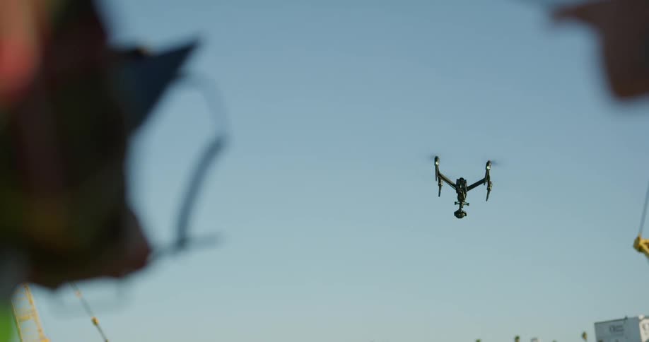 Two people standing with a drone in the sky with trees in the background