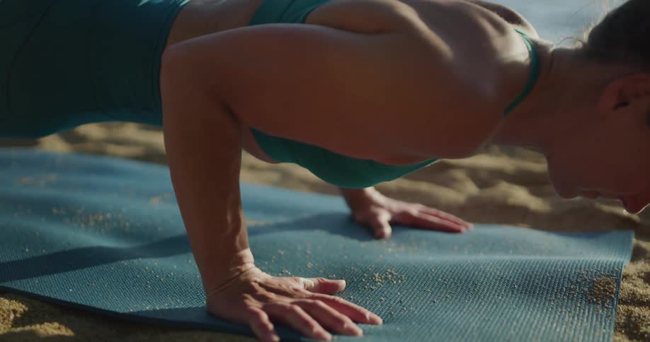 Fit woman practices yoga over a mat in the sand near the lake at sunset