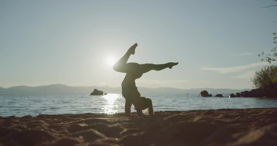 Young fit woman practices yoga on the sands near a lake in the mountains at sunset