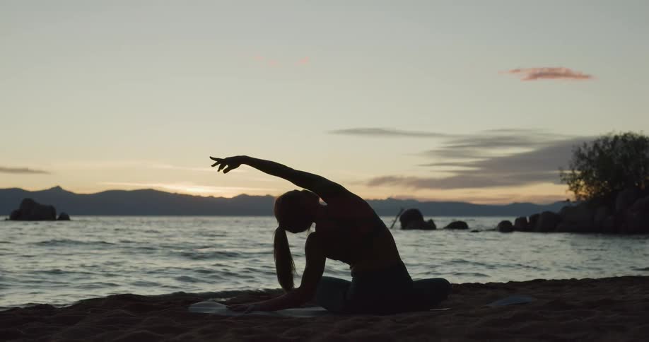 A woman sitting on the shore and stretching with the sky and clouds in the background