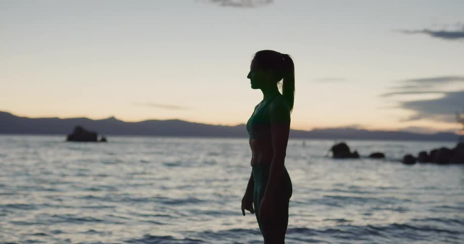 A woman looks out over the ocean while standing on the beach at sunset