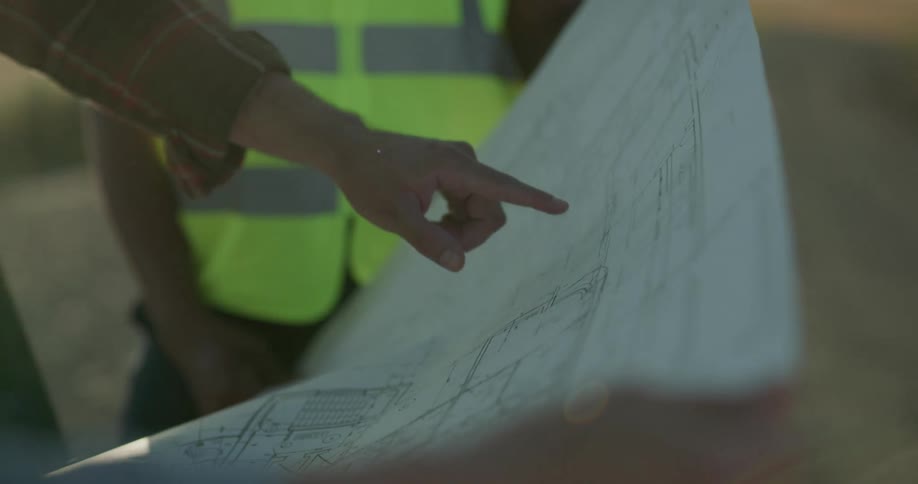 Three men each wearing safety vests and hard hats look at building plans