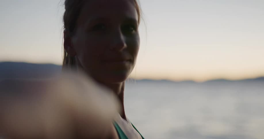 Fit woman practices yoga near a lake on the mountains at sunset