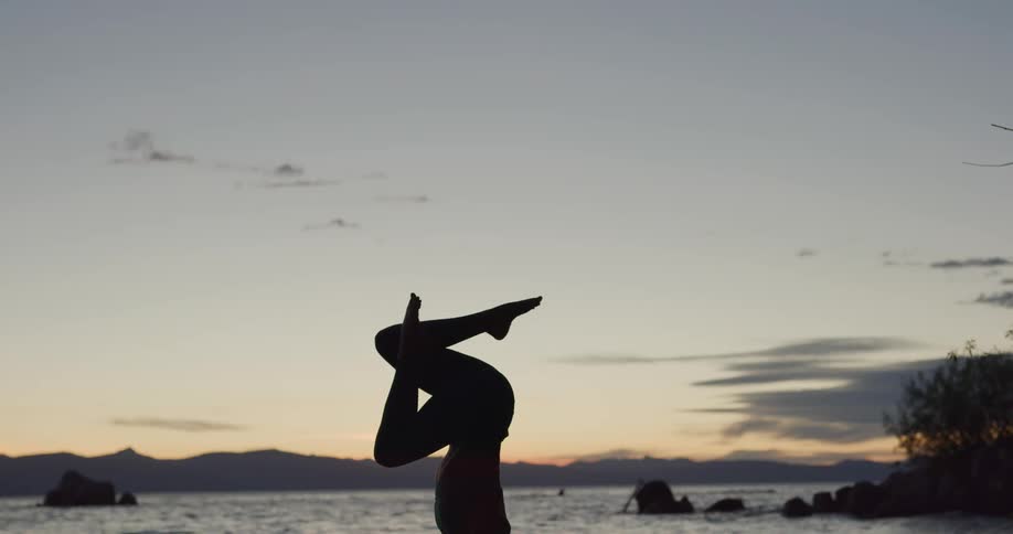 A woman is doing yoga at the beach while the sun is setting
