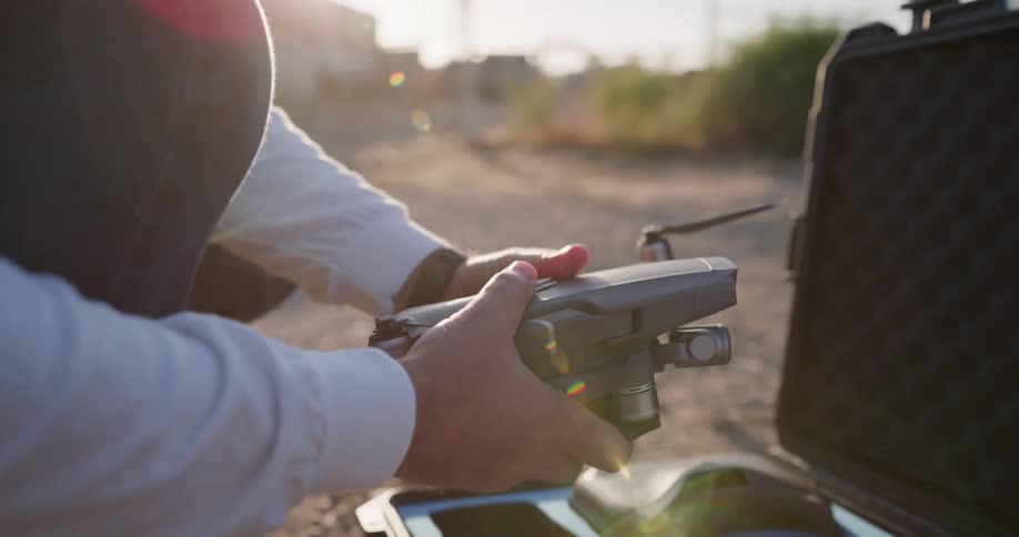 A person stooping down taking drone parts from a suitcase with plants and the sky in the background
