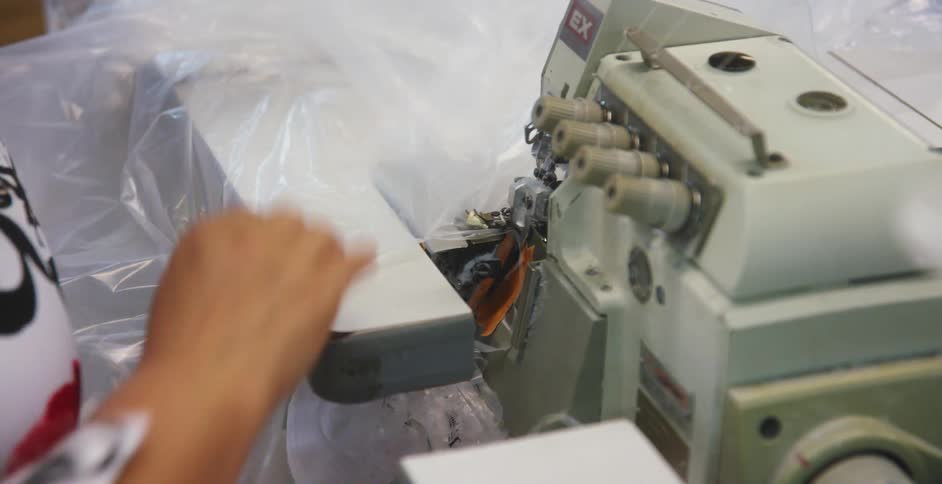 A woman feeds a large sheet of plastic into a machine that cuts the sheet into thin slits