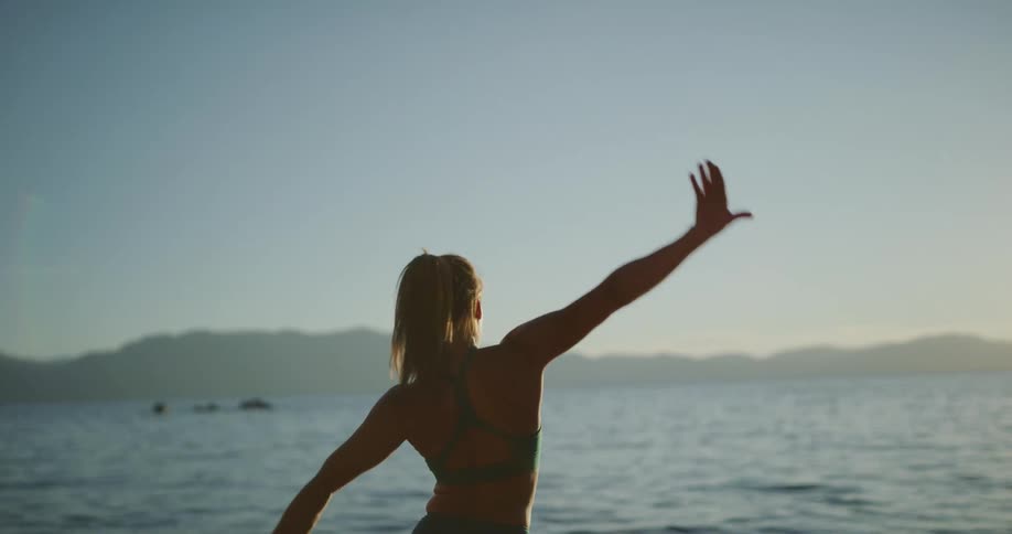 A young woman does yoga in front of the water