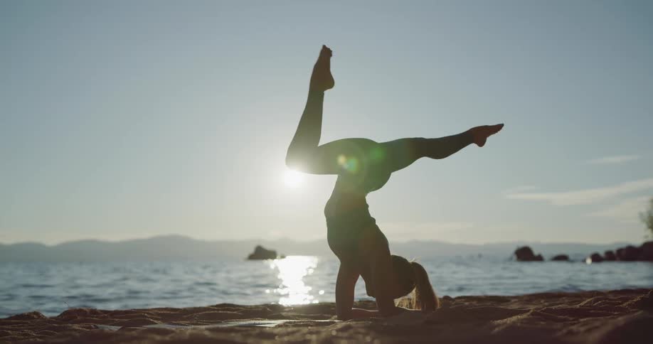 A woman does yoga on the beach next to the ocean