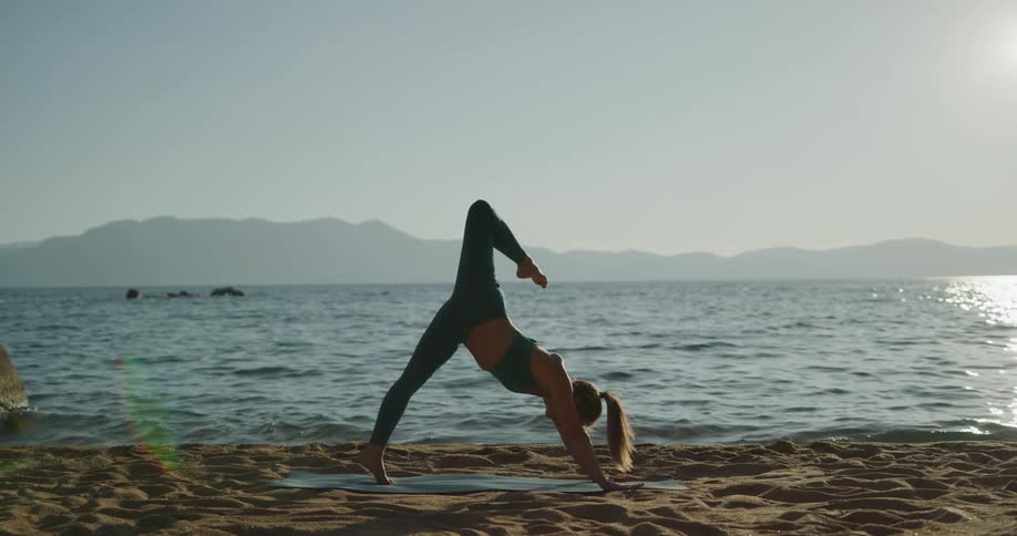 A woman is doing yoga at the beach while the sun is setting