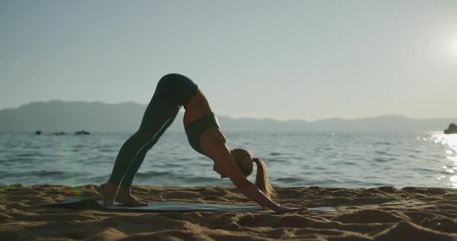 Fit woman practices yoga over a mat in the shores of a lake in the mountains
