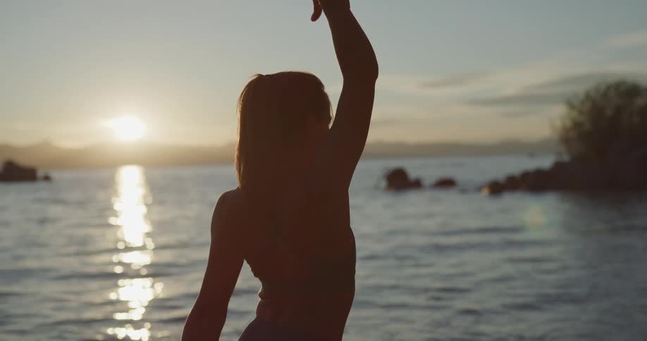 A woman standing on the shore and stretching with the sky and clouds in the background