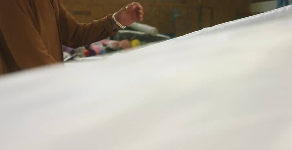 A man with a hat and mask smoothing out a sheet of plastic with a wooden stick