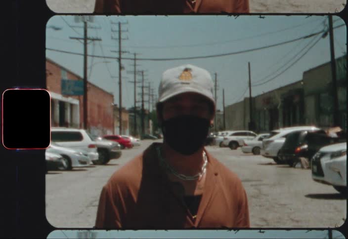 Man wearing a cap and a mask stands near parked cars