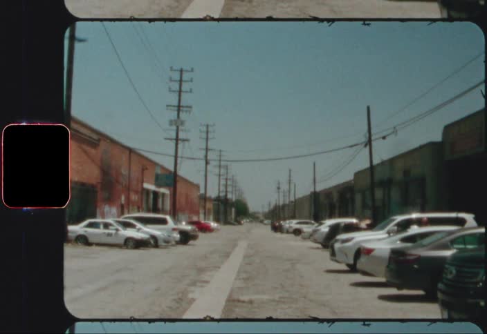A couple dozen vehicles are parked in an alley running between a business district in a small town
