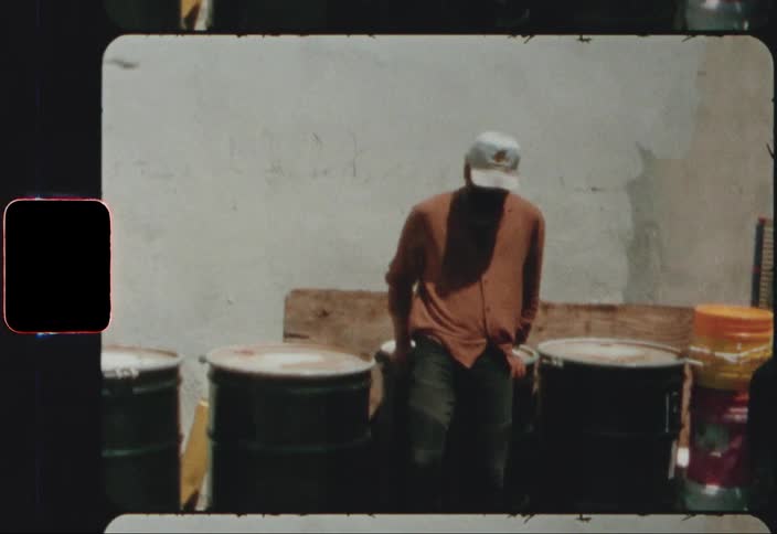 A man walks over to a row of oil barrels and jumps on one and poses