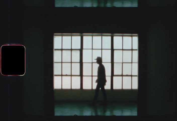 A man in a baseball cap walks past a large gridded window in a building