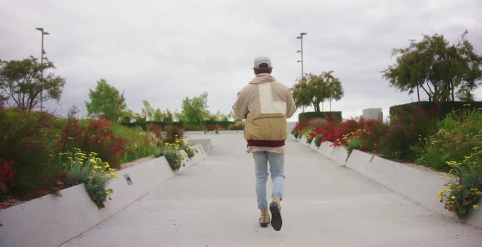 Young man wearing a jacket walks on a path surrounded by flowers in a park