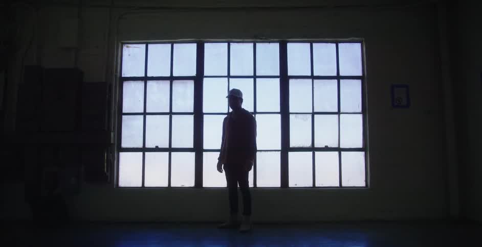 A man stands in front of a large grid window in a deserted building