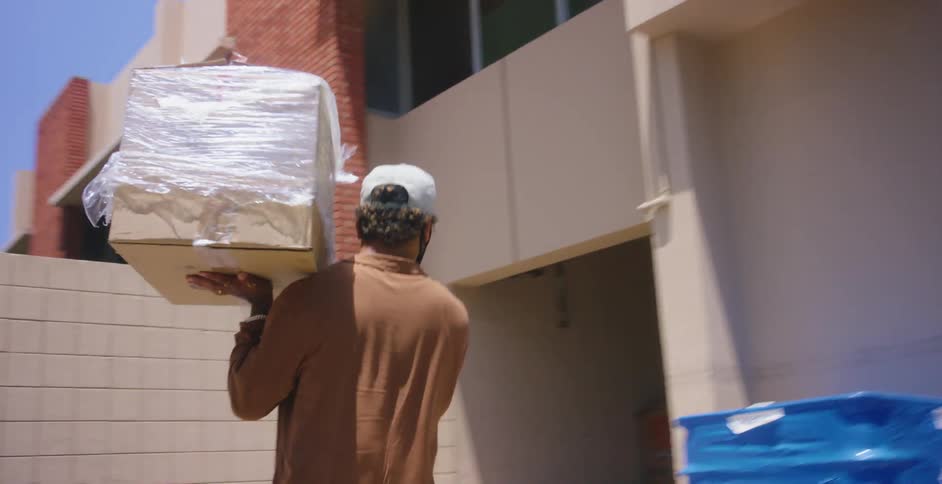 Man wearing a face mask carries a cardboard box into a warehouse