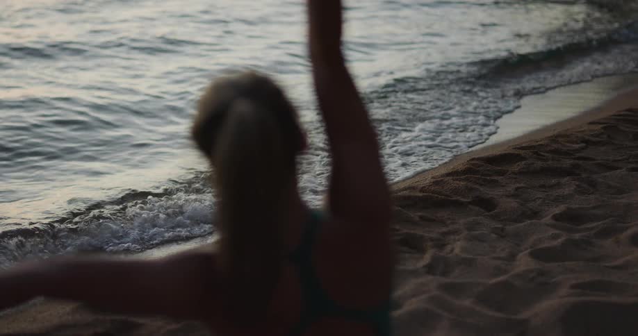 Fit woman practices yoga over the sands of a lake shore in the mountain at sunset