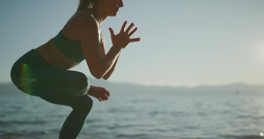 Woman practices yoga on the sand of a lake shoreline in the mountains