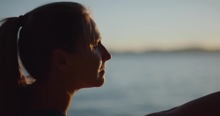 Woman performs yoga as ocean reflects sun sitting on horizon