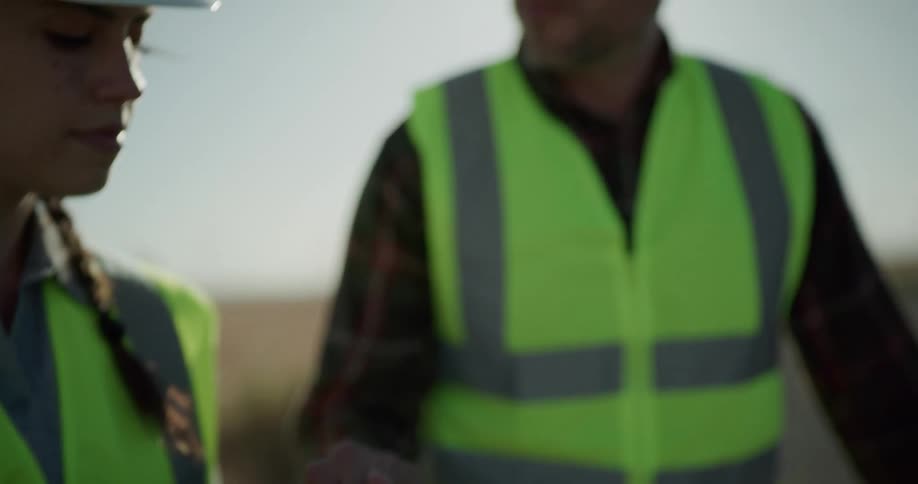Supervisors wearing white hard hats and vests talk on a construction site