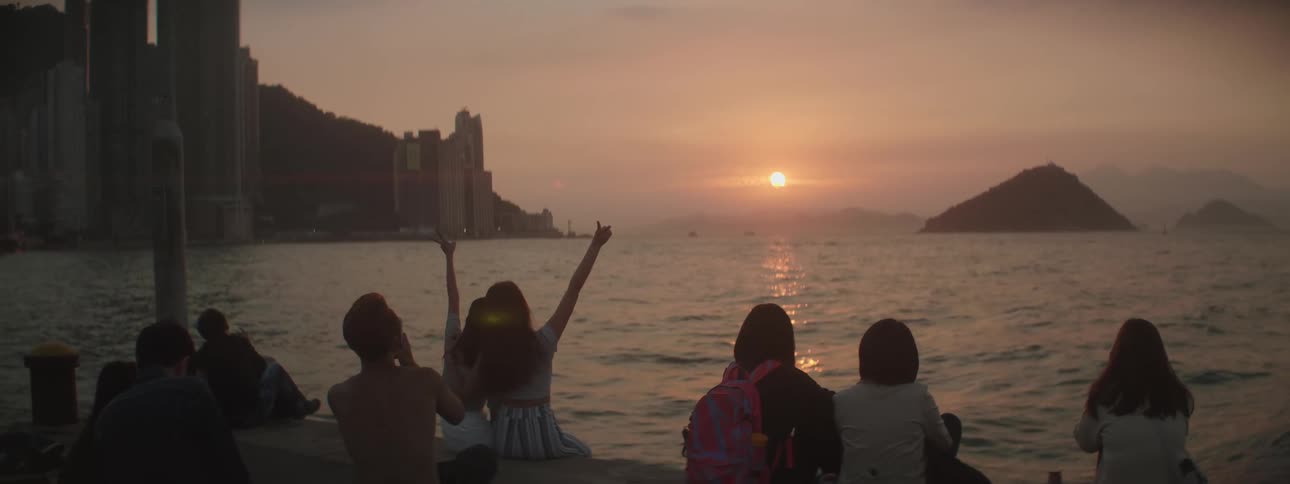 Sun sinks toward horizon turning sky red behind downtown city and mountain as people sit on docks watching and filming