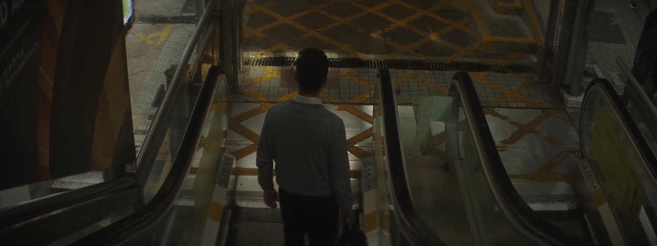 Young man carrying a bag steps out of an escalator in a mall
