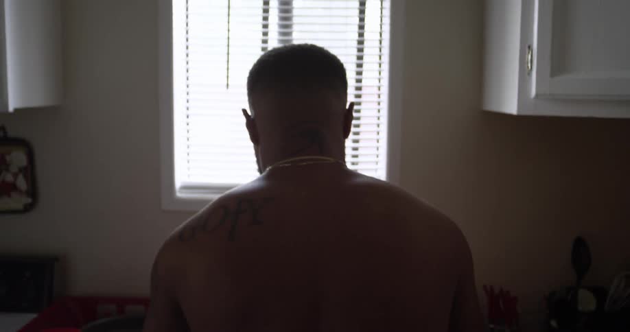 A man with a tattoo on his back stands near a window