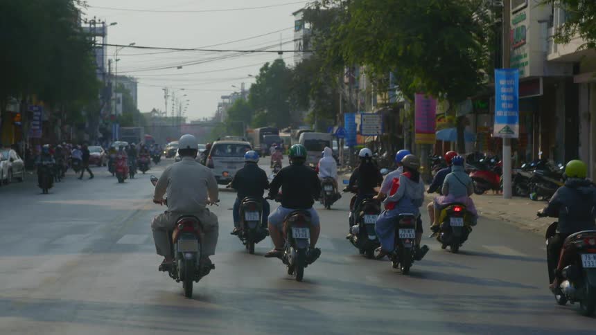 Pedestrians cross a city street as a large group of people on motorcycles drive by
