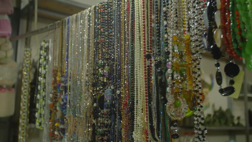 Numerous necklaces hang while on display from a rod mounted in a shop