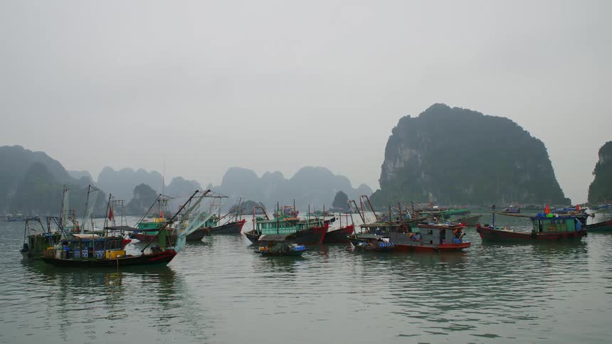 A group of colorful boats floating on the ocean between tall rock formations on a foggy day