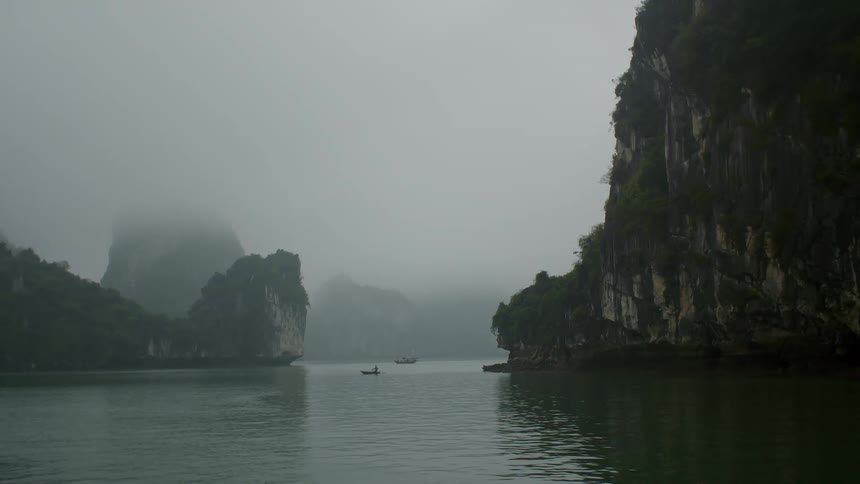 Two boats float on calm water between rocky cliffs
