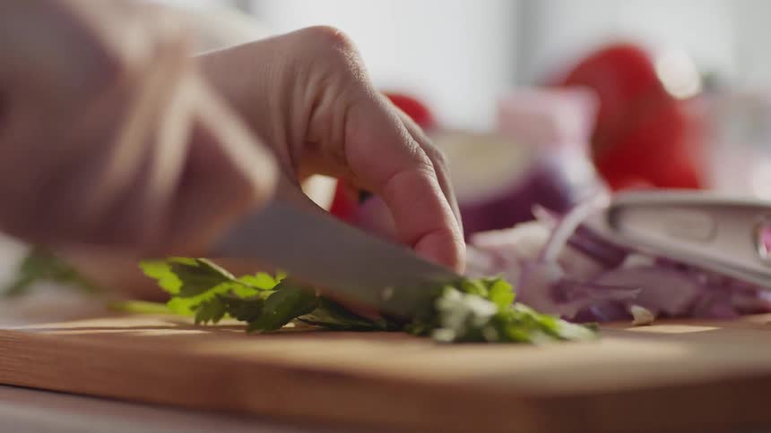A woman chopping parsley on a wood cutting board in a kitchen