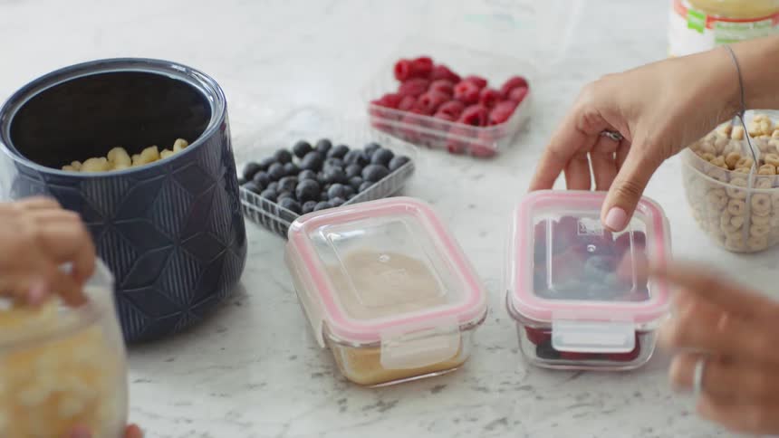 A woman and her child pack fruit and snacks in containers