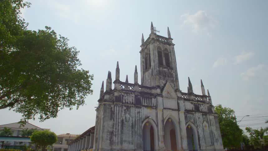 A church next to a large tree with buildings the sky and clouds in the background