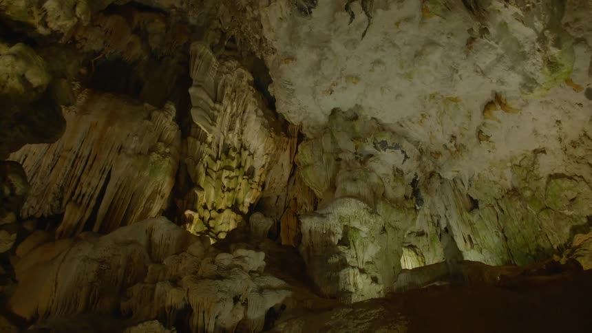 Green lights shine on the stalagmites and stalactites inside a cavern