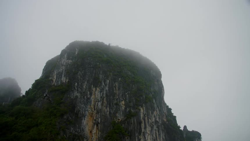 Steep cliffs of a mountain covered in vegetation under the clouds