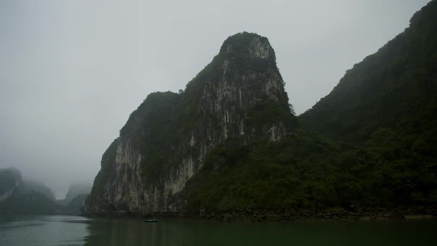 A green canoe floats in the ocean near a tall promontory covered in vegetation