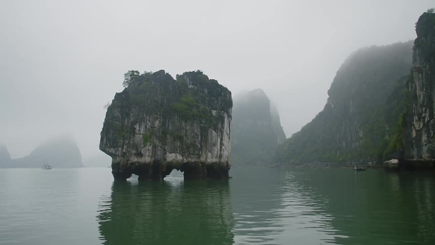 A large coastal rock formation surrounded by ocean water on a misty day